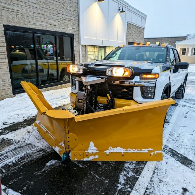 Heavy duty yellow snow plow blade on a modern white truck, clearing a parking area in winter